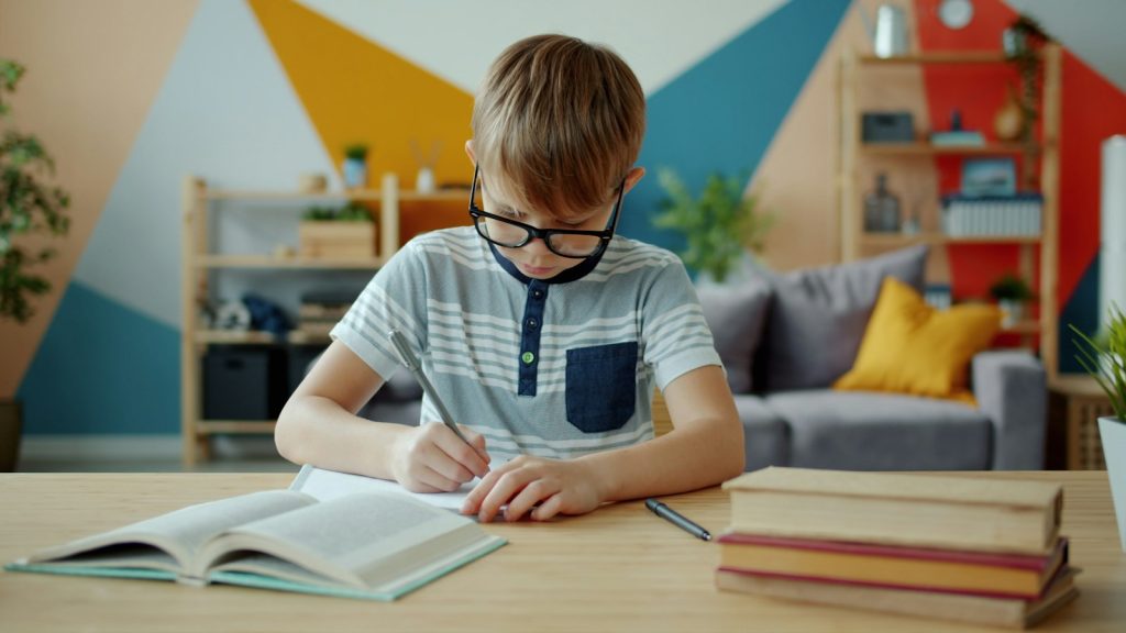 Young boy writing in a notebook at a desk